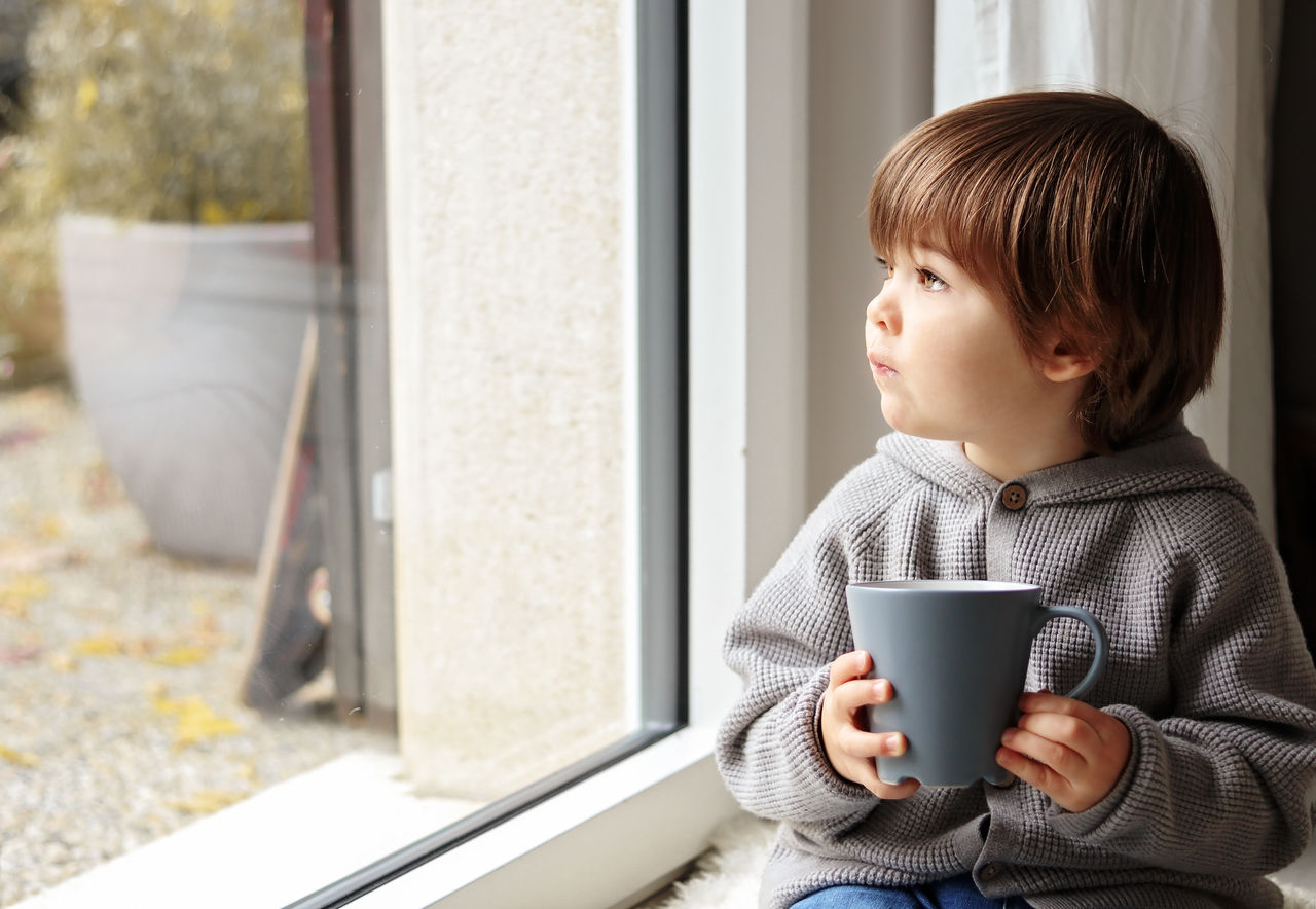 Kleinkind hält Becher in der Hand und schaut aus dem Fenster