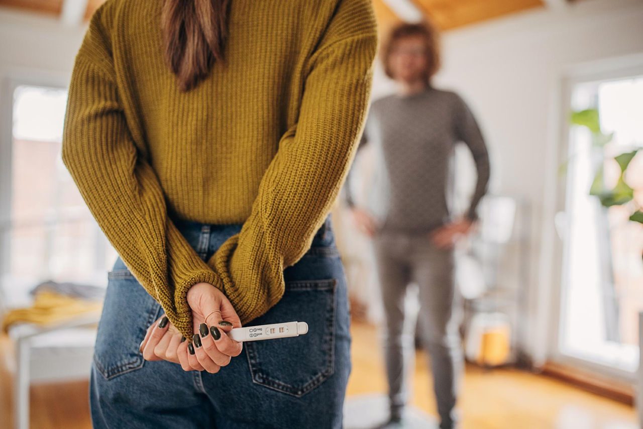Schwangere Frau hält Schwangerschaftstest hinter dem Rücken